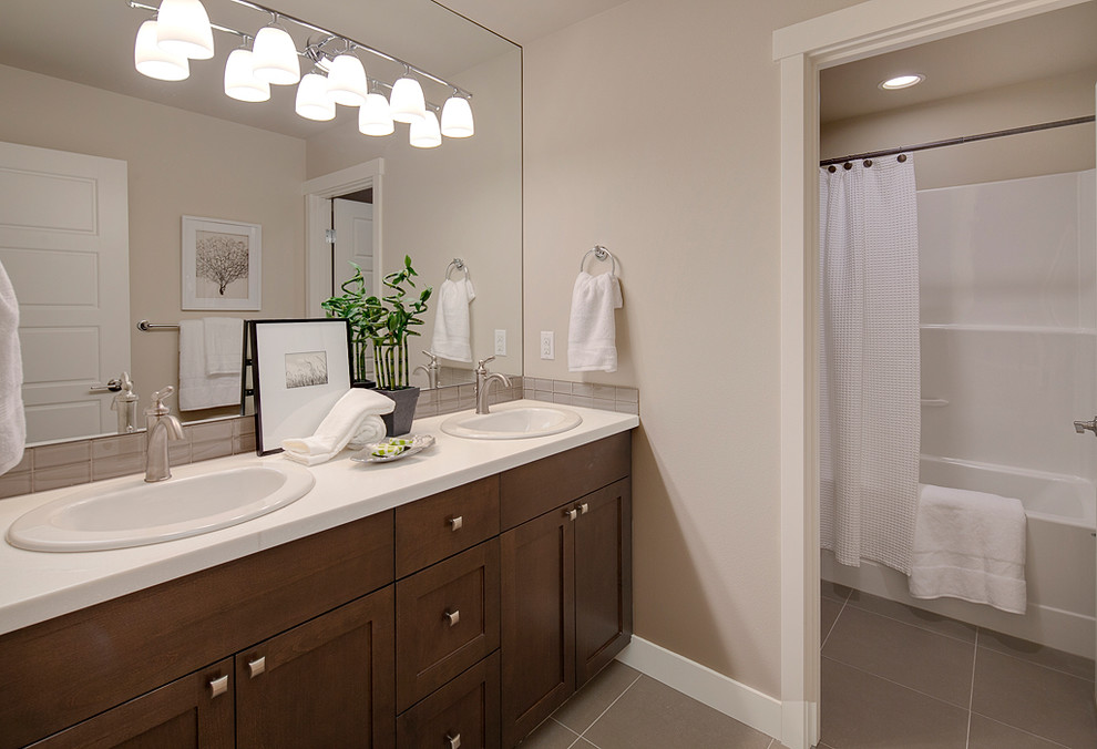 Arts and crafts kids bathroom in Seattle with a drop-in sink, recessed-panel cabinets, medium wood cabinets, solid surface benchtops, an alcove tub, a shower/bathtub combo, gray tile, glass tile, beige walls, porcelain floors and a two-piece toilet.