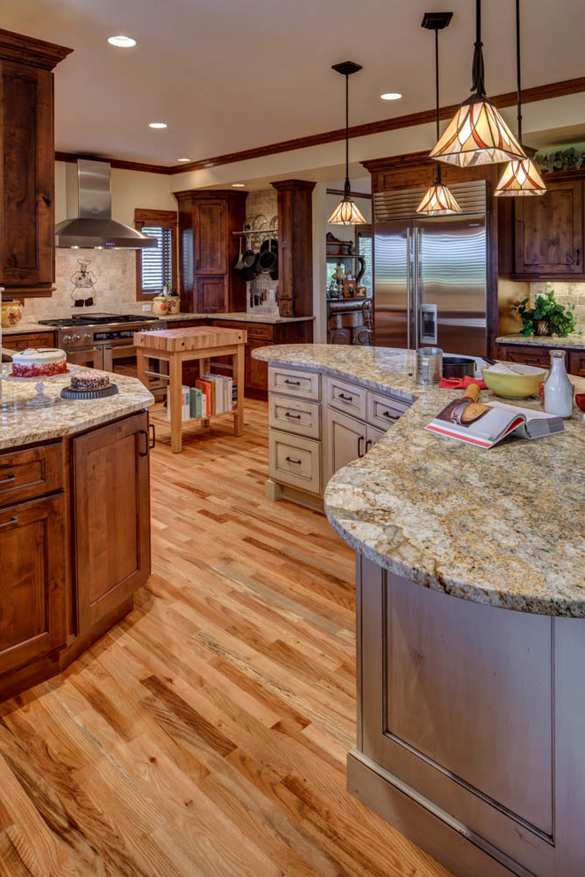 Design ideas for a large traditional u-shaped eat-in kitchen in Denver with an undermount sink, recessed-panel cabinets, brown cabinets, granite benchtops, grey splashback, stone tile splashback, stainless steel appliances, light hardwood floors and multiple islands.