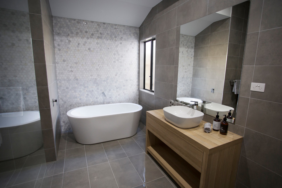 Photo of a mid-sized contemporary bathroom in Melbourne with light wood cabinets, gray tile, laminate benchtops, a freestanding tub, ceramic tile, grey walls, ceramic floors, a vessel sink, a double shower and an open shower.