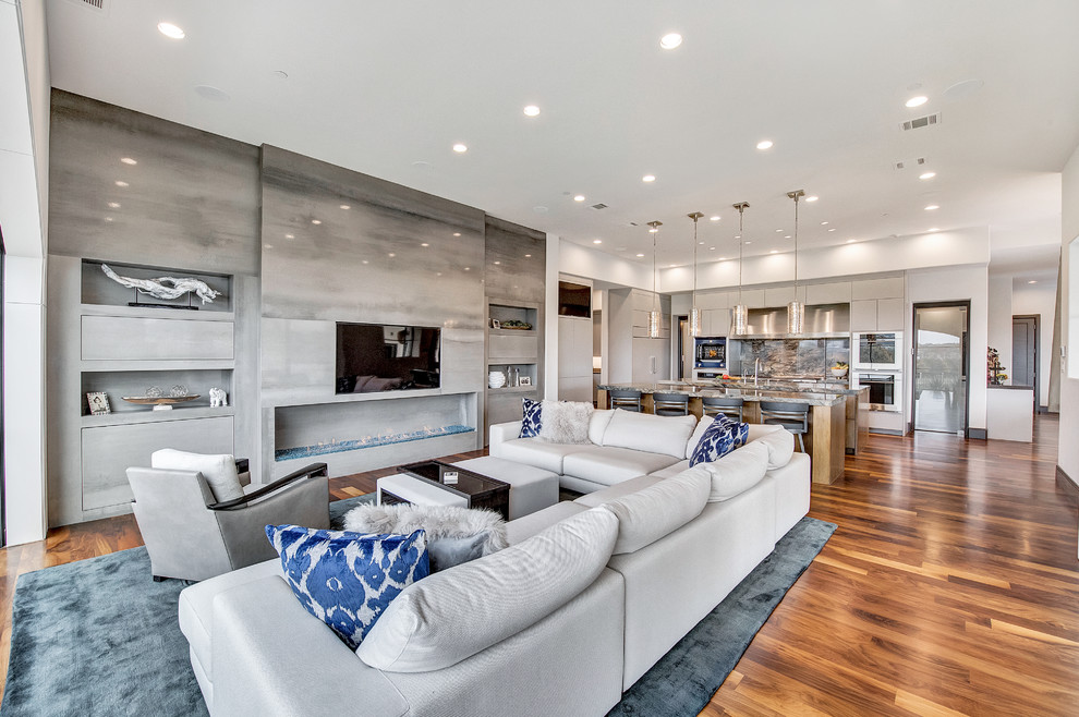 Expansive contemporary open concept family room in Orange County with white walls, medium hardwood floors, a standard fireplace, a stone fireplace surround, a built-in media wall and brown floor.