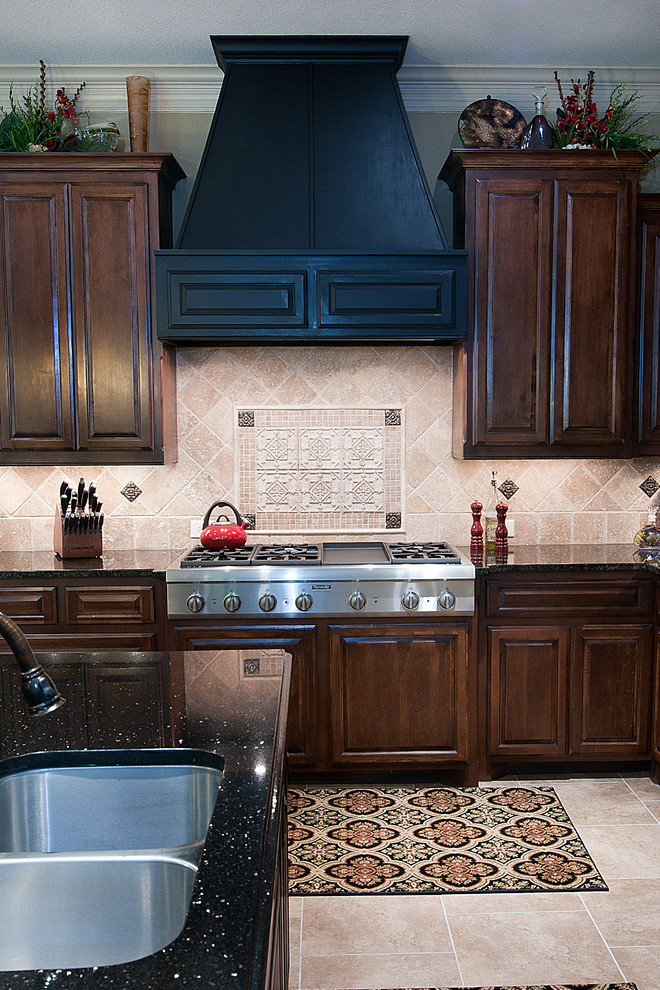 Open concept kitchen - large traditional l-shaped ceramic tile open concept kitchen idea with a double-bowl sink, raised-panel cabinets, dark wood cabinets, granite countertops, beige backsplash, stone tile backsplash, stainless steel appliances, beige walls and an island