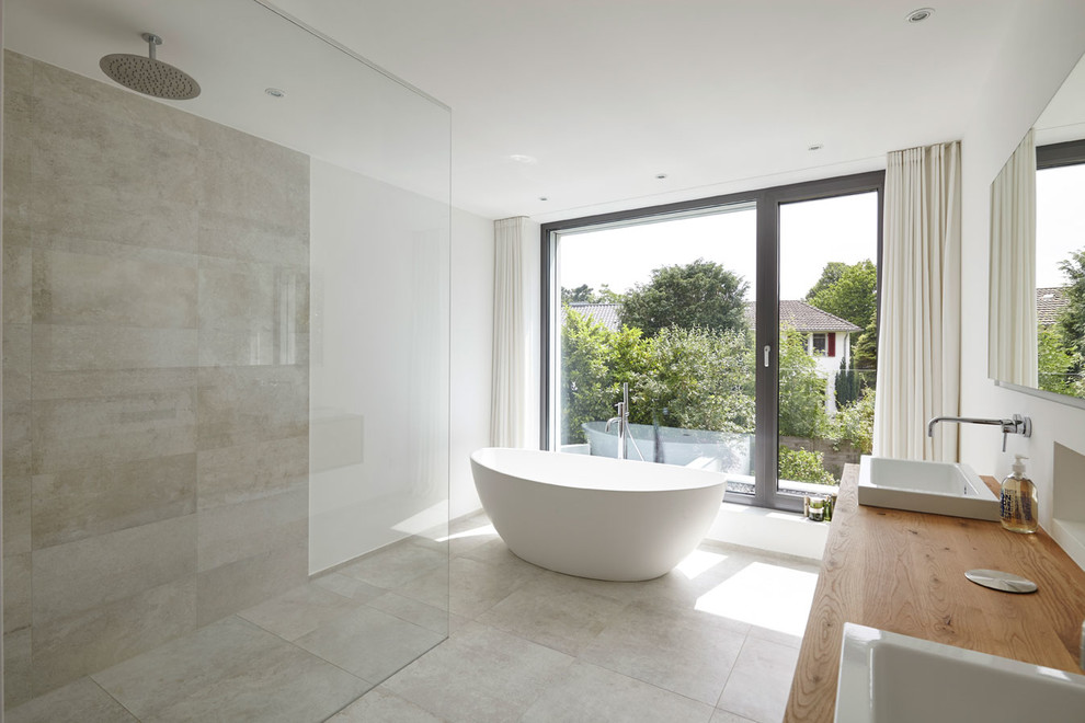 Duschbad With flächenbündigen Schrankfronten, hellen Holzschränken, freistehender Badewanne, bodengleicher Dusche, beigen Fliesen, Kalkfliesen, beiger Wandfarbe, Aufsatzwaschbecken, Waschtisch aus Holz and offener Dusche in Cologne