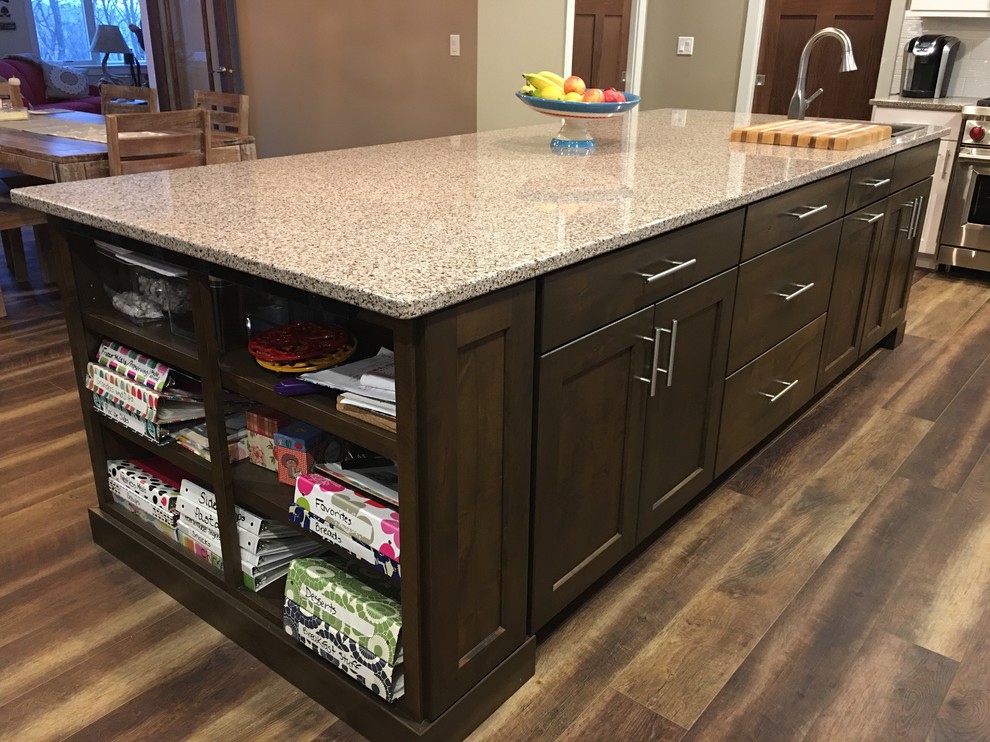 Example of a large transitional l-shaped dark wood floor and brown floor eat-in kitchen design with a farmhouse sink, shaker cabinets, white cabinets, granite countertops, white backsplash, stainless steel appliances and an island