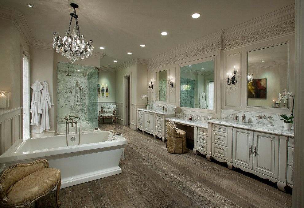 Inspiration for an expansive transitional master bathroom in Phoenix with an undermount sink, raised-panel cabinets, white cabinets, a freestanding tub, a corner shower, white tile, dark hardwood floors, a two-piece toilet, stone slab, beige walls, marble benchtops and beige floor.