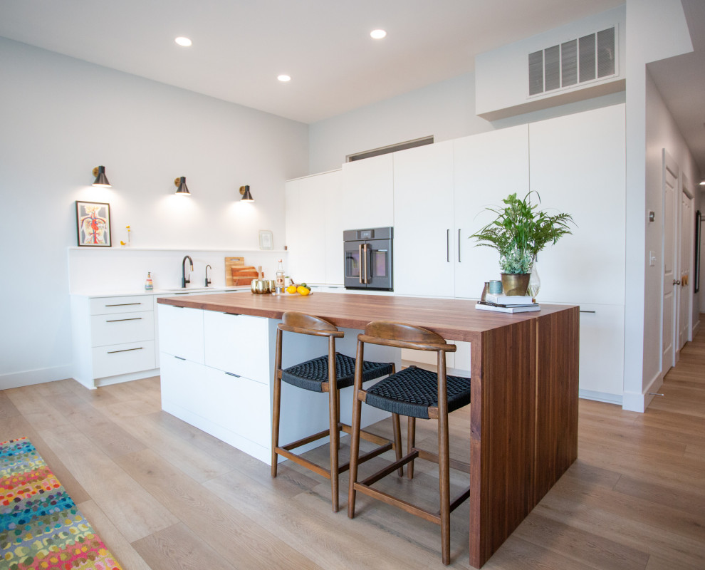 Photo of a small scandinavian l-shaped open plan kitchen in Columbus with a submerged sink, flat-panel cabinets, white cabinets, engineered stone countertops, white splashback, stainless steel appliances, laminate floors, an island and white worktops.