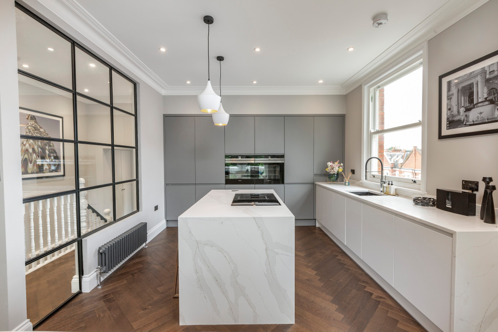 Inspiration for a mid-sized contemporary single-wall open plan kitchen in London with a drop-in sink, grey cabinets, black appliances, with island, white benchtop, flat-panel cabinets, grey splashback, medium hardwood floors and brown floor.