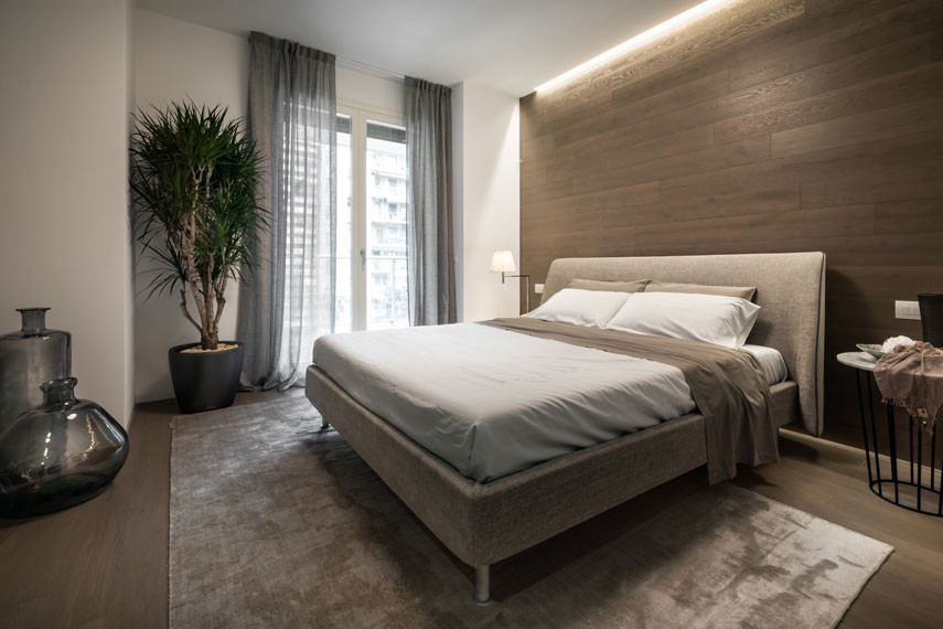 Photo of a large modern master bedroom in Milan with beige walls, light hardwood floors, brown floor and wood walls.