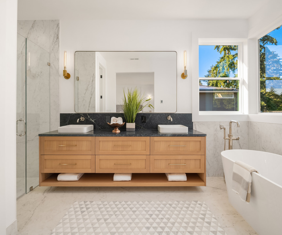 Design ideas for a medium sized traditional ensuite bathroom in Seattle with shaker cabinets, light wood cabinets, a freestanding bath, a built-in shower, a one-piece toilet, white tiles, porcelain tiles, white walls, porcelain flooring, a vessel sink, soapstone worktops, white floors, a hinged door, black worktops, a wall niche, double sinks and a floating vanity unit.