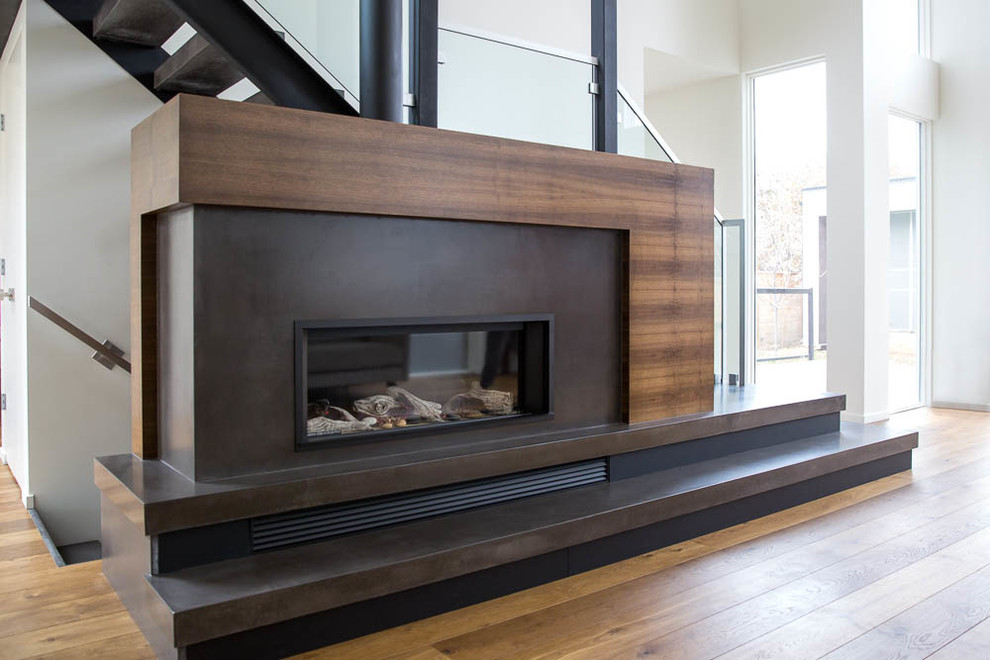 Mid-sized modern open concept living room in Calgary with a library, white walls, medium hardwood floors, a wood stove, a concrete fireplace surround and no tv.