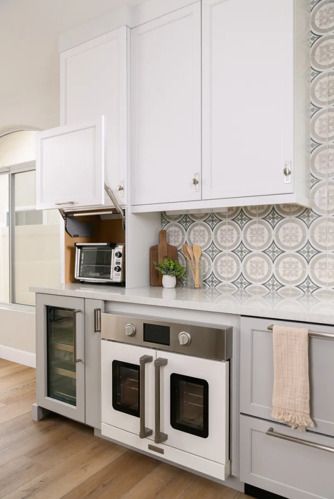 Eat-in kitchen - transitional l-shaped vinyl floor and brown floor eat-in kitchen idea in Orange County with a farmhouse sink, shaker cabinets, gray cabinets, quartz countertops, multicolored backsplash, porcelain backsplash, stainless steel appliances, an island and white countertops