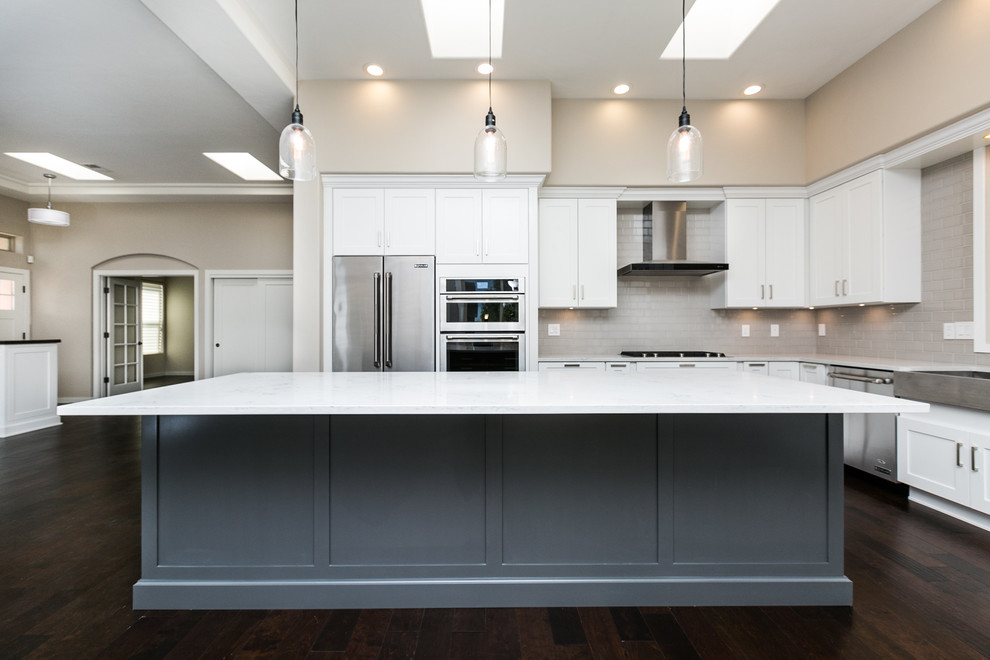 Example of a large transitional l-shaped dark wood floor and brown floor eat-in kitchen design in Albuquerque with a farmhouse sink, shaker cabinets, white cabinets, quartz countertops, gray backsplash, subway tile backsplash, stainless steel appliances and an island