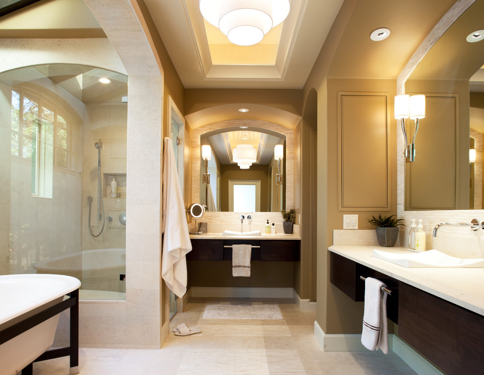 Photo of a large mediterranean master bathroom in San Francisco with a drop-in sink, flat-panel cabinets, dark wood cabinets, a freestanding tub, a curbless shower, white tile, beige walls, limestone floors and granite benchtops.