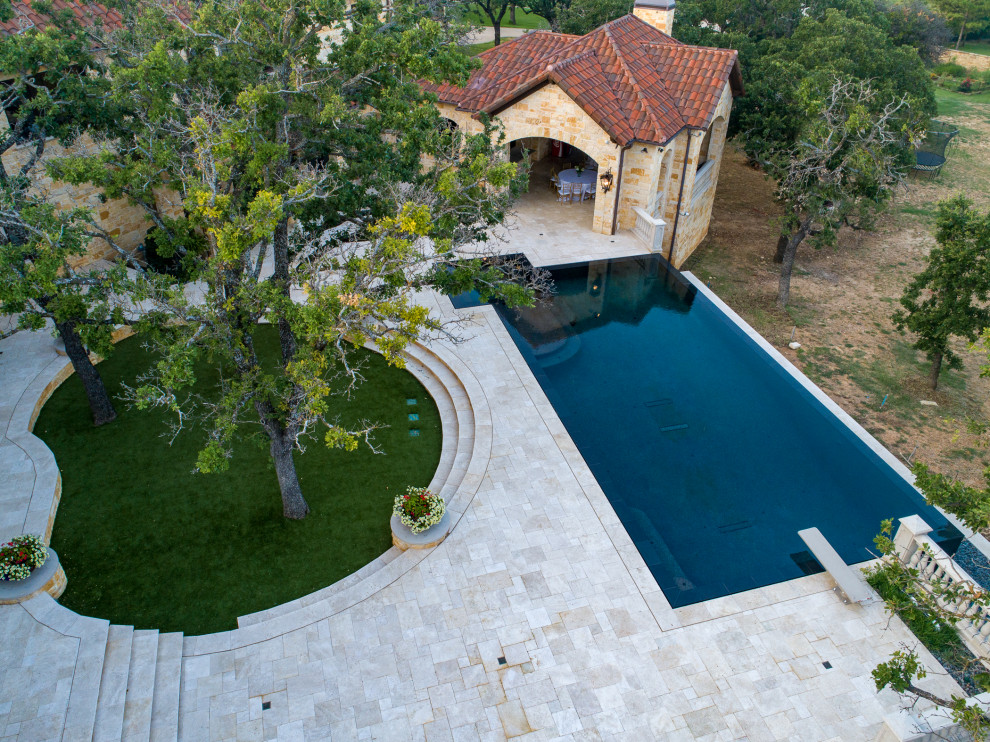 Esempio di una grande piscina a sfioro infinito country personalizzata dietro casa con pavimentazioni in pietra naturale