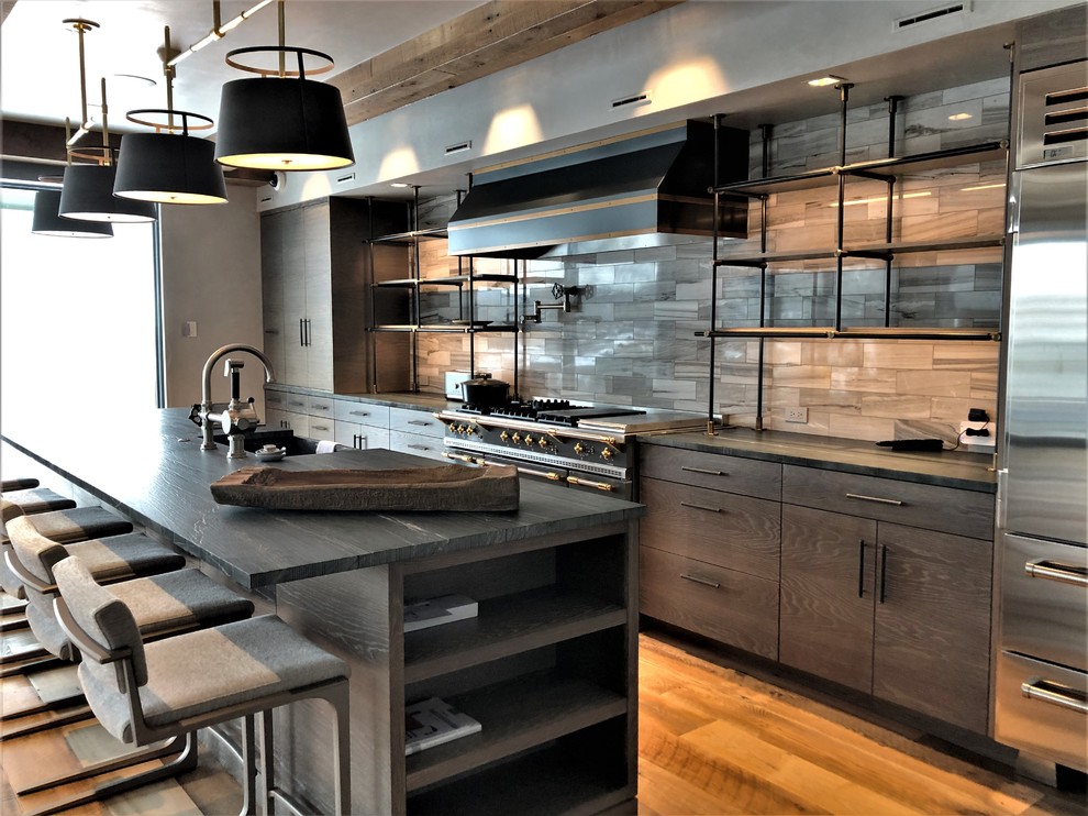 Large contemporary u-shaped eat-in kitchen in Denver with a farmhouse sink, flat-panel cabinets, light wood cabinets, quartzite benchtops, beige splashback, porcelain splashback, stainless steel appliances, medium hardwood floors, with island, brown floor and black benchtop.