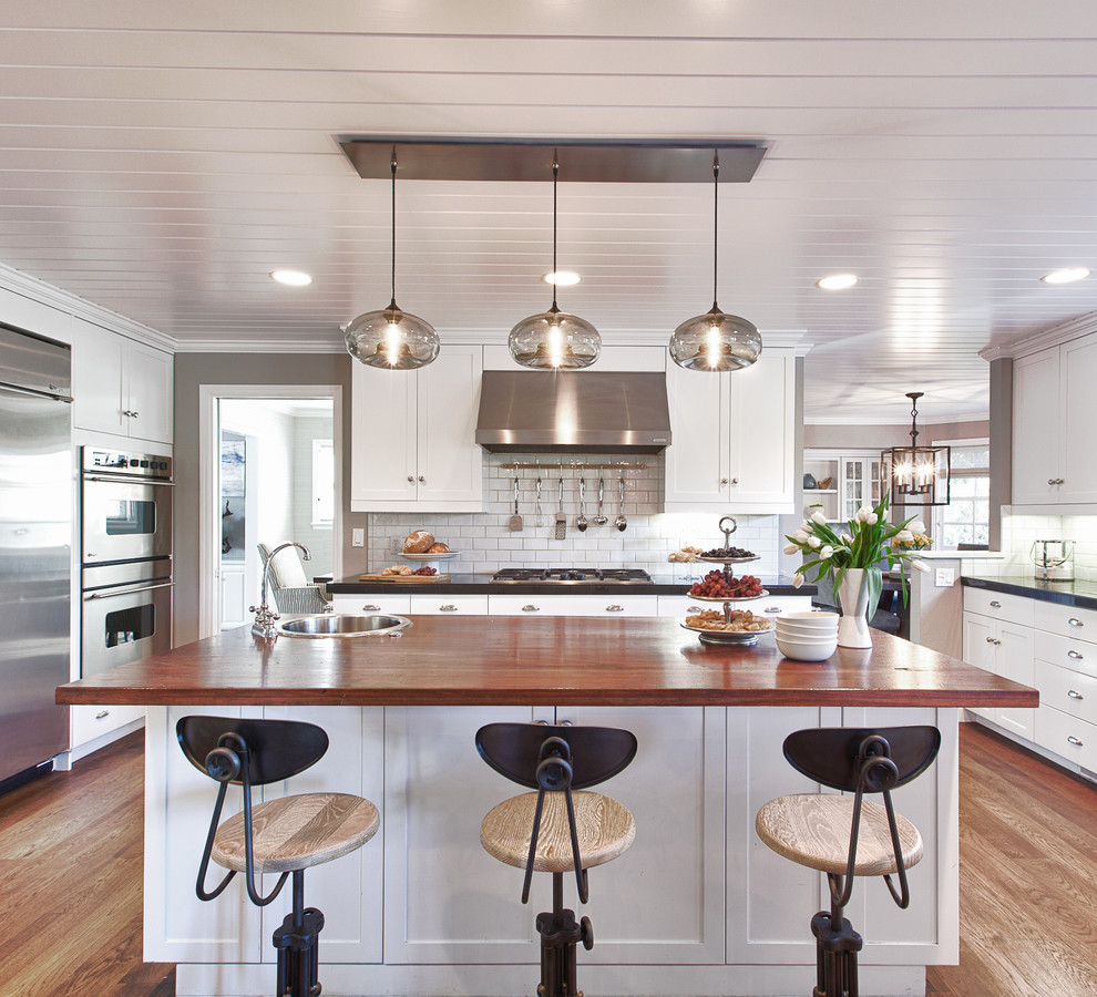 Large contemporary u-shaped eat-in kitchen in San Francisco with wood benchtops, shaker cabinets, white cabinets, white splashback, stainless steel appliances, medium hardwood floors, with island, subway tile splashback and brown floor.