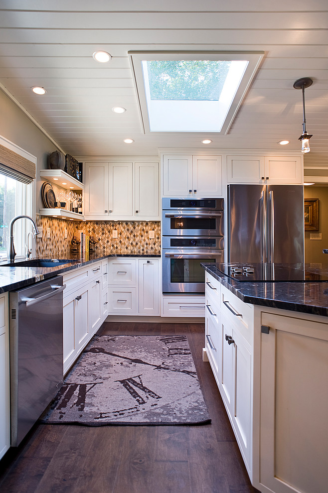Open concept kitchen - mid-sized transitional l-shaped medium tone wood floor and brown floor open concept kitchen idea with an undermount sink, recessed-panel cabinets, white cabinets, granite countertops, multicolored backsplash, mosaic tile backsplash, stainless steel appliances and an island