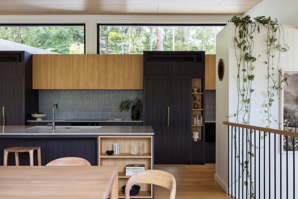 This is an example of a mid-sized contemporary galley eat-in kitchen in Sydney with an undermount sink, flat-panel cabinets, dark wood cabinets, quartz benchtops, mosaic tile splashback, black appliances, light hardwood floors, with island, grey splashback, beige floor, grey benchtop and wood.