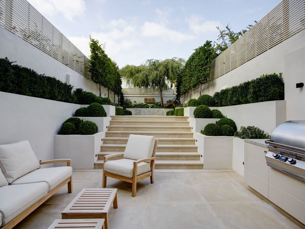 This is an example of a contemporary backyard patio in London with natural stone pavers and no cover.