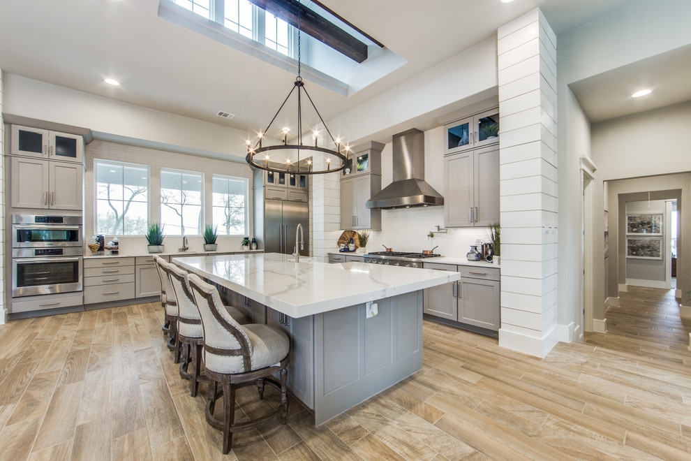 Inspiration for a large country eat-in kitchen in Dallas with a farmhouse sink, shaker cabinets, grey cabinets, quartz benchtops, white splashback, ceramic splashback, stainless steel appliances, porcelain floors, multiple islands and beige floor.