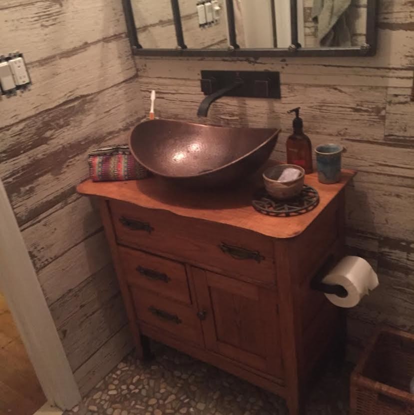 This is an example of a mid-sized country 3/4 bathroom in New York with recessed-panel cabinets, medium wood cabinets, a two-piece toilet, brown walls, pebble tile floors, a vessel sink, wood benchtops and multi-coloured floor.