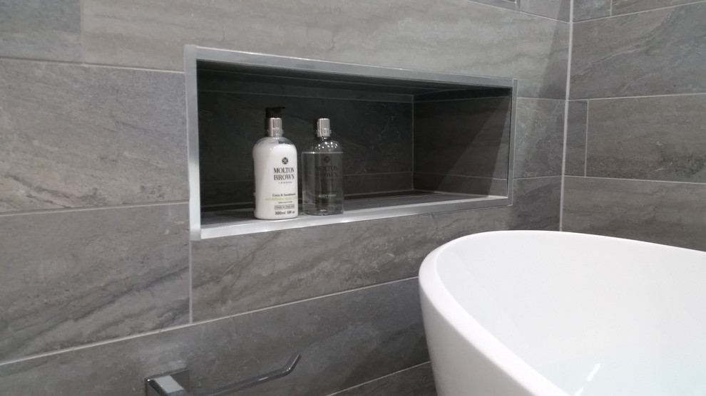 Modelo de cuarto de baño minimalista de tamaño medio con bañera exenta, ducha abierta, sanitario de pared, baldosas y/o azulejos grises, baldosas y/o azulejos de porcelana, paredes blancas y suelo de baldosas de porcelana