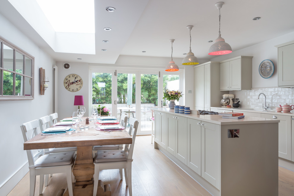 This is an example of a transitional kitchen in London with shaker cabinets, grey cabinets, white splashback, subway tile splashback and light hardwood floors.