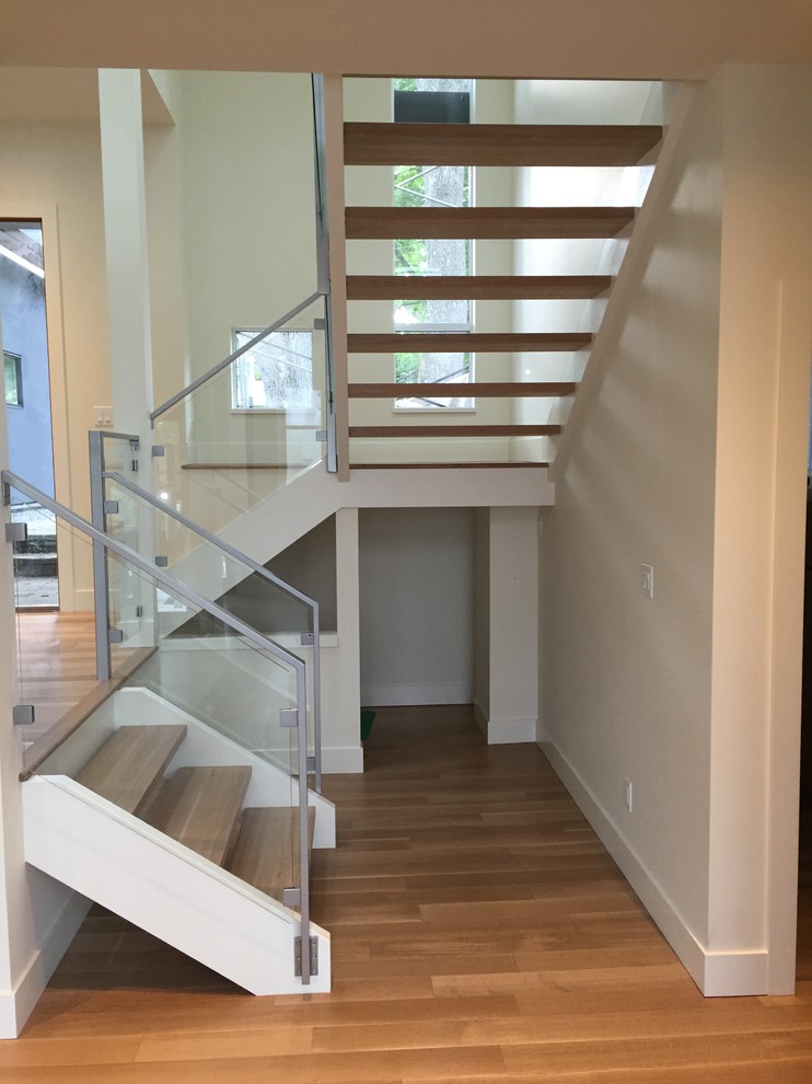 This is an example of a large contemporary wood u-shaped staircase in Vancouver with open risers and glass railing.