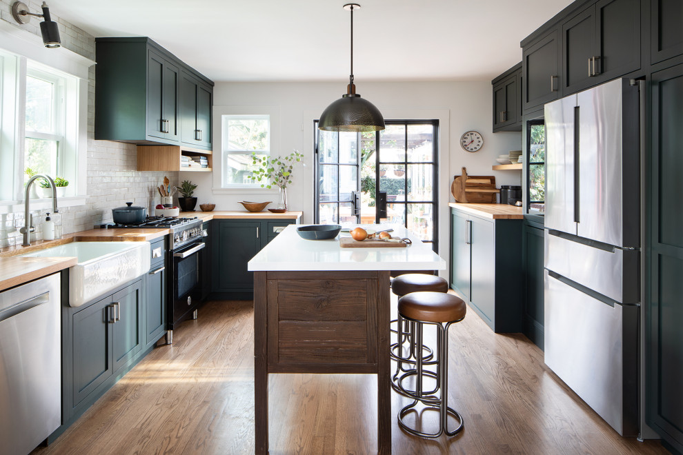 This is an example of a medium sized traditional u-shaped enclosed kitchen in San Francisco with a belfast sink, shaker cabinets, green cabinets, wood worktops, white splashback, terracotta splashback, black appliances, medium hardwood flooring, an island, brown floors and brown worktops.