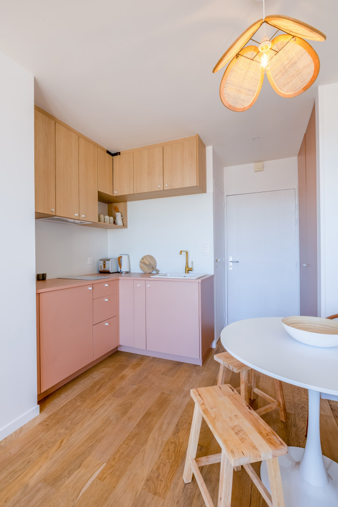 На фото: угловая кухня-гостиная в белых тонах с отделкой деревом в скандинавском стиле с врезной мойкой, светлыми деревянными фасадами, светлым паркетным полом и розовой столешницей с