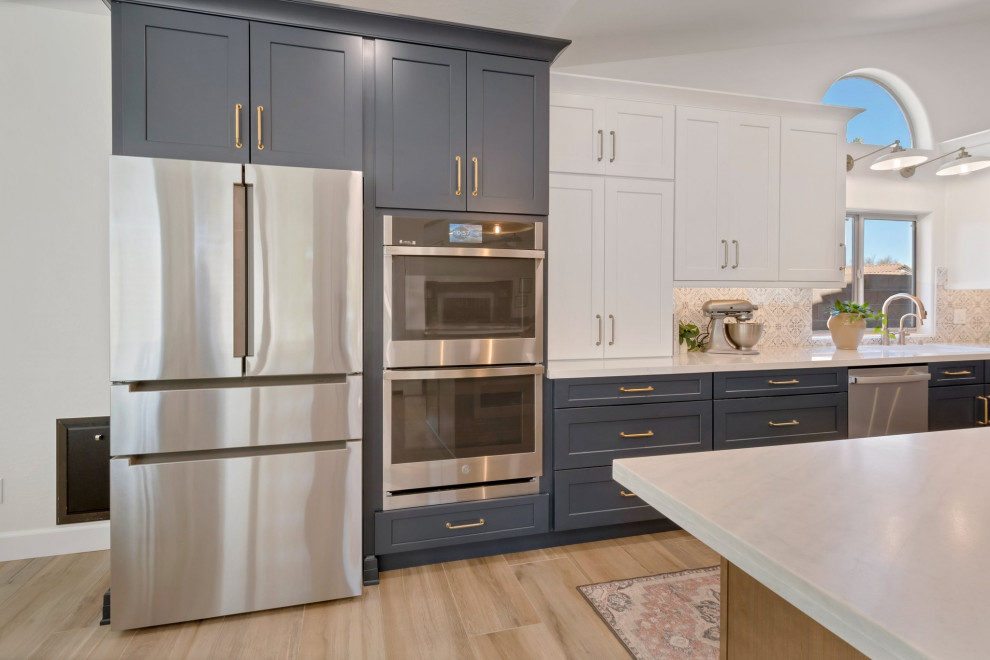 Large transitional l-shaped porcelain tile, brown floor and vaulted ceiling eat-in kitchen photo in Phoenix with an undermount sink, shaker cabinets, blue cabinets, quartzite countertops, multicolored backsplash, mosaic tile backsplash, stainless steel appliances, two islands and white countertops