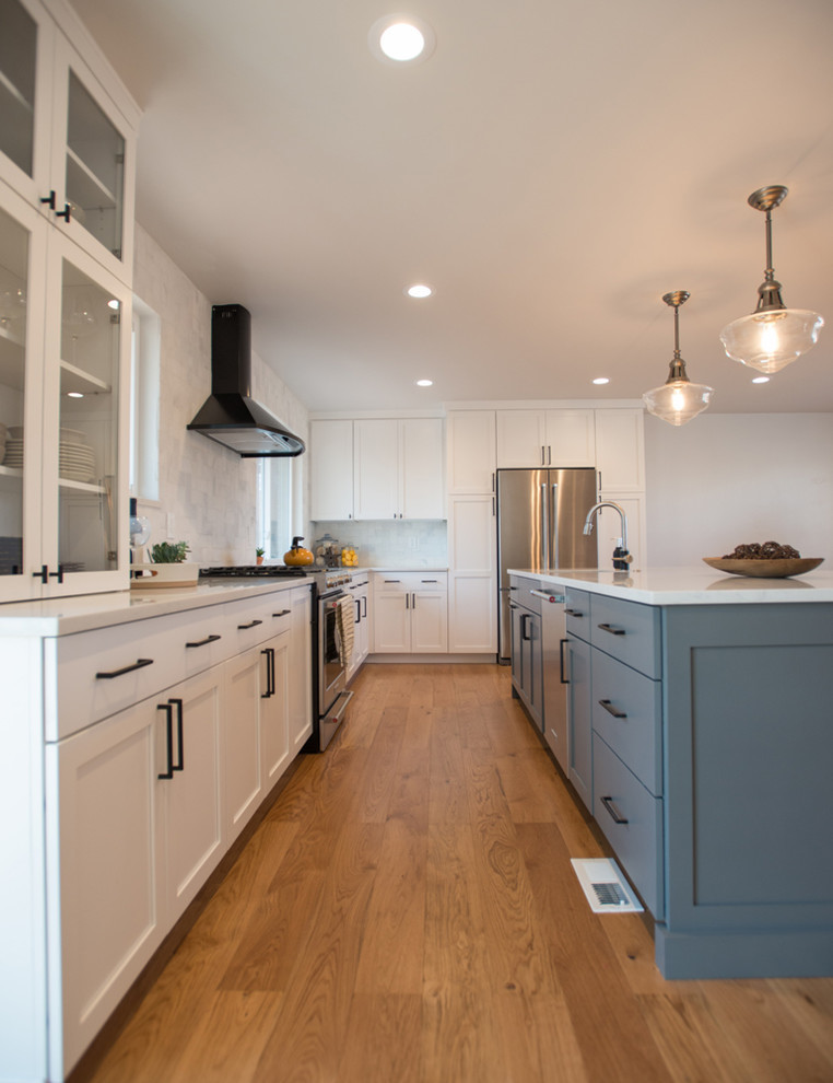 This is an example of a mid-sized contemporary galley eat-in kitchen in Denver with an undermount sink, glass-front cabinets, beige cabinets, quartz benchtops, white splashback, ceramic splashback, stainless steel appliances, medium hardwood floors and with island.