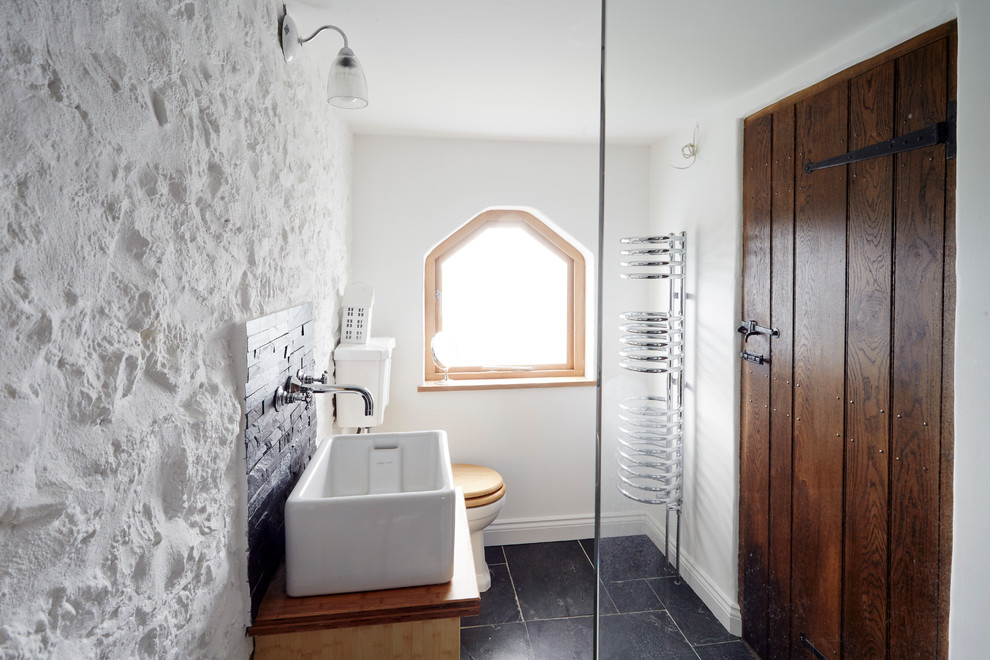 Inspiration for a small country bathroom in Wiltshire with a trough sink, wood benchtops, a two-piece toilet, black tile, stone tile, white walls, limestone floors and brown benchtops.