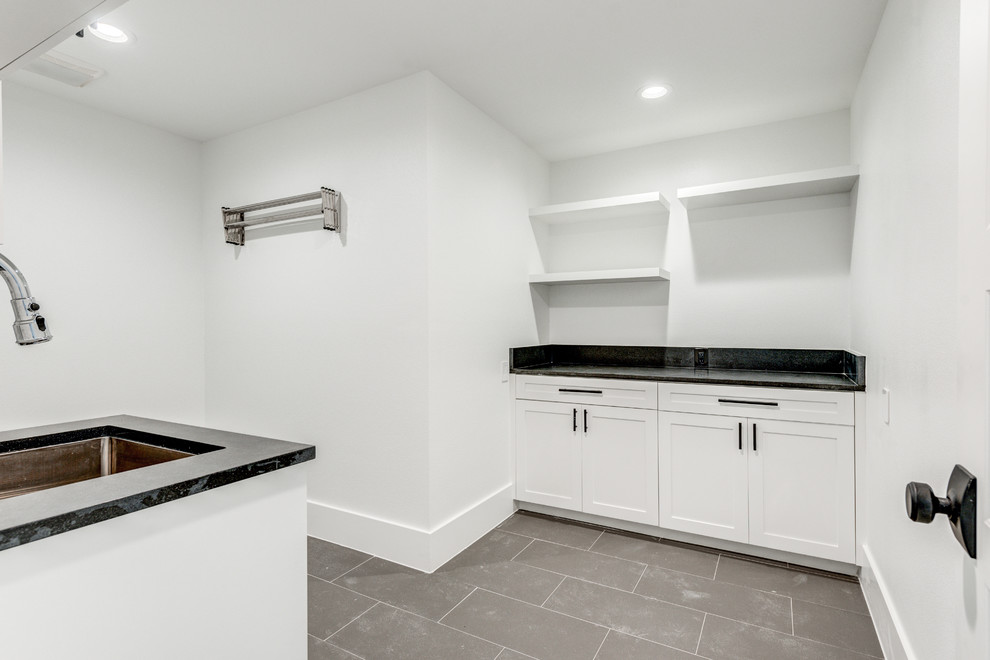 Large modern l-shaped utility room in Dallas with an undermount sink, shaker cabinets, white cabinets, granite benchtops, white walls, porcelain floors, a side-by-side washer and dryer, grey floor and black benchtop.