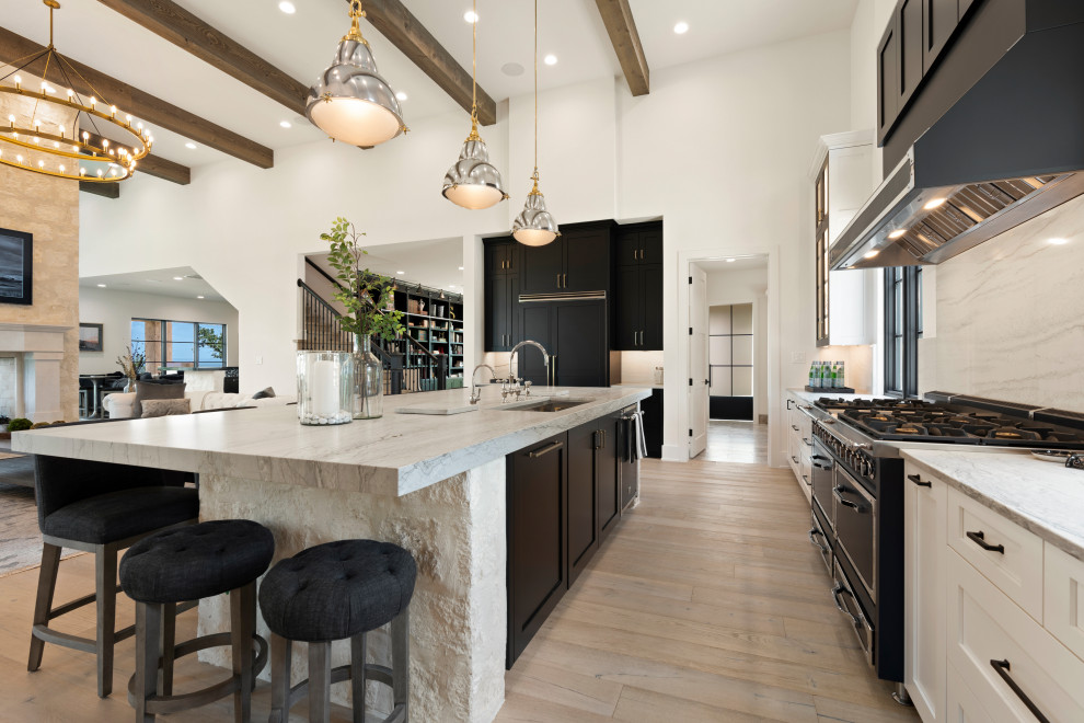 Huge l-shaped open concept kitchen photo with white cabinets, marble countertops, white backsplash, marble backsplash, black appliances, an island and gray countertops
