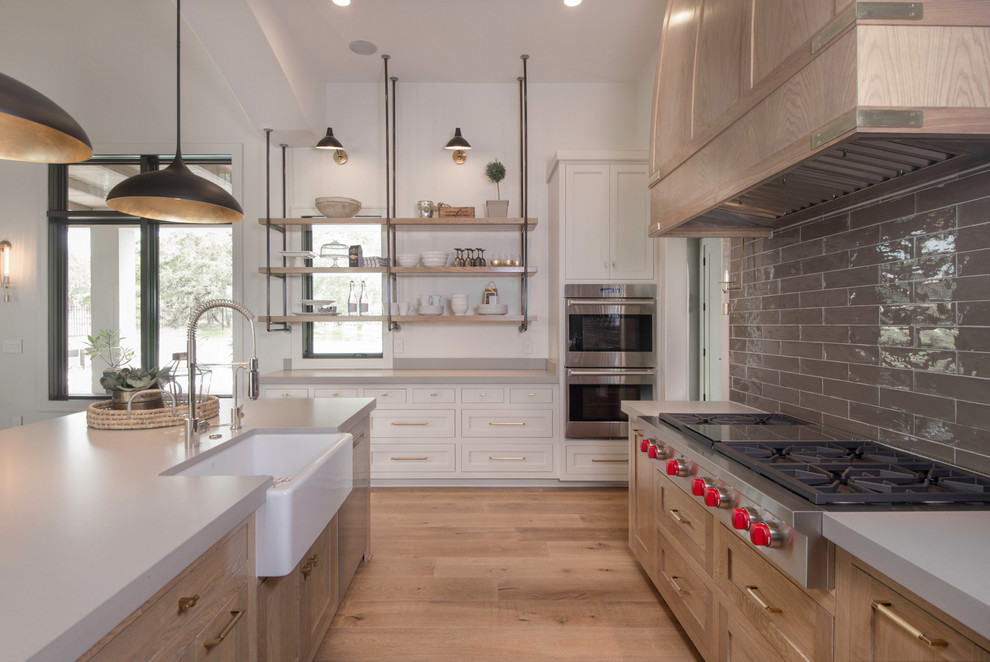 This is an example of a transitional kitchen in Austin with a farmhouse sink, shaker cabinets, light wood cabinets, brown splashback, stainless steel appliances, light hardwood floors and with island.