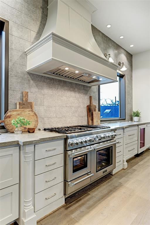 Inspiration for an expansive transitional u-shaped separate kitchen in Houston with a farmhouse sink, shaker cabinets, grey cabinets, quartz benchtops, grey splashback, brick splashback, stainless steel appliances, light hardwood floors, with island, brown floor, grey benchtop and exposed beam.
