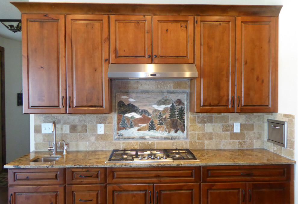 Inspiration for a mid-sized rustic single-wall medium tone wood floor and brown floor eat-in kitchen remodel in Denver with an undermount sink, raised-panel cabinets, brown cabinets, granite countertops, beige backsplash, travertine backsplash, stainless steel appliances, an island and multicolored countertops