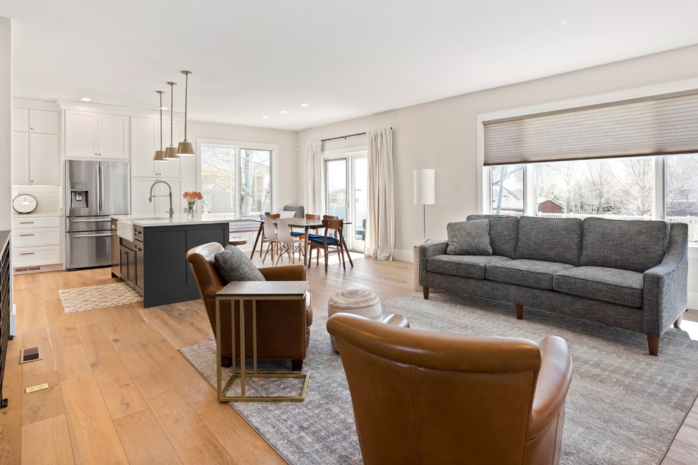 Transitional l-shaped light wood floor and brown floor kitchen photo with a farmhouse sink, shaker cabinets, white cabinets, quartz countertops, white backsplash, subway tile backsplash, stainless steel appliances, an island and white countertops