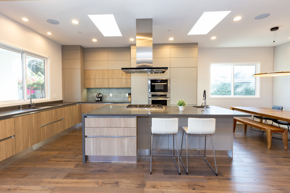 Mid-sized contemporary l-shaped open plan kitchen in San Francisco with an undermount sink, flat-panel cabinets, brown cabinets, quartz benchtops, blue splashback, stainless steel appliances, medium hardwood floors, with island, brown floor and grey benchtop.