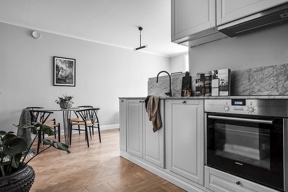 Design ideas for a scandinavian l-shaped eat-in kitchen in Stockholm with a double-bowl sink, white cabinets, marble benchtops, white splashback, marble splashback, stainless steel appliances and no island.
