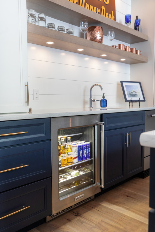 Example of a mid-sized beach style galley medium tone wood floor and brown floor wet bar design in Milwaukee with an undermount sink, flat-panel cabinets, white cabinets, quartz countertops, white backsplash, shiplap backsplash and white countertops