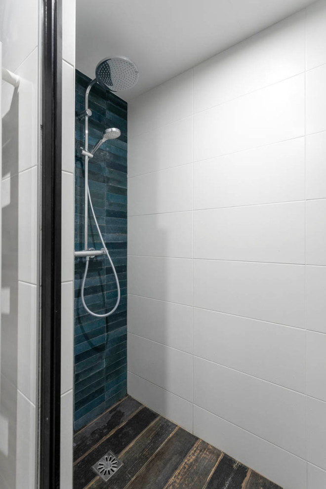 Bild på ett mellanstort funkis brun brunt en-suite badrum, med släta luckor, grå skåp, en dusch i en alkov, en vägghängd toalettstol, blå kakel, porslinskakel, vita väggar, klinkergolv i terrakotta, ett nedsänkt handfat, träbänkskiva, grått golv och dusch med gångjärnsdörr