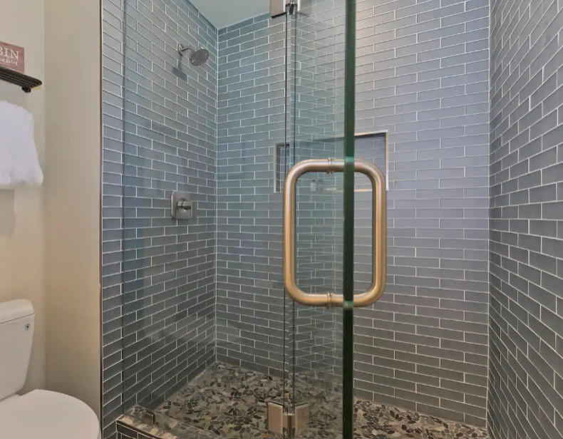 This is an example of a small transitional master bathroom in Other with shaker cabinets, brown cabinets, an alcove shower, a two-piece toilet, white tile, glass tile, white walls, pebble tile floors, an undermount sink, quartzite benchtops, brown floor, a hinged shower door, white benchtops, a niche, a double vanity and a freestanding vanity.
