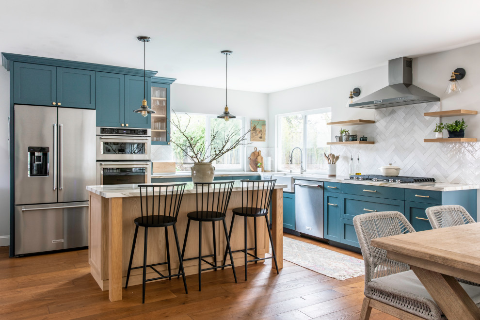 Photo of a medium sized farmhouse l-shaped kitchen/diner in San Francisco with a belfast sink, shaker cabinets, light wood cabinets, ceramic splashback, stainless steel appliances, dark hardwood flooring, an island, brown floors and white worktops.