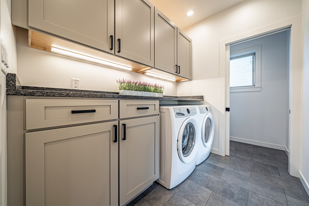 Photo of a mid-sized contemporary single-wall utility room in Other with shaker cabinets, grey cabinets, granite benchtops, grey splashback, granite splashback, white walls, ceramic floors, an integrated washer and dryer, grey floor and grey benchtop.