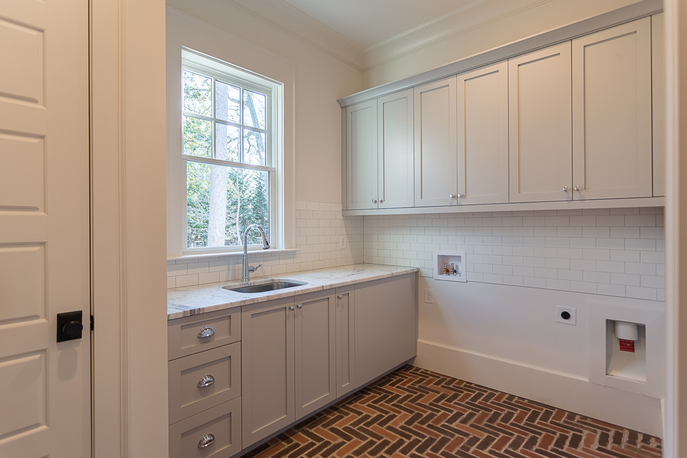 Design ideas for a mid-sized transitional l-shaped dedicated laundry room in Atlanta with an undermount sink, shaker cabinets, grey cabinets, marble benchtops, white walls, brick floors, a side-by-side washer and dryer and brown floor.