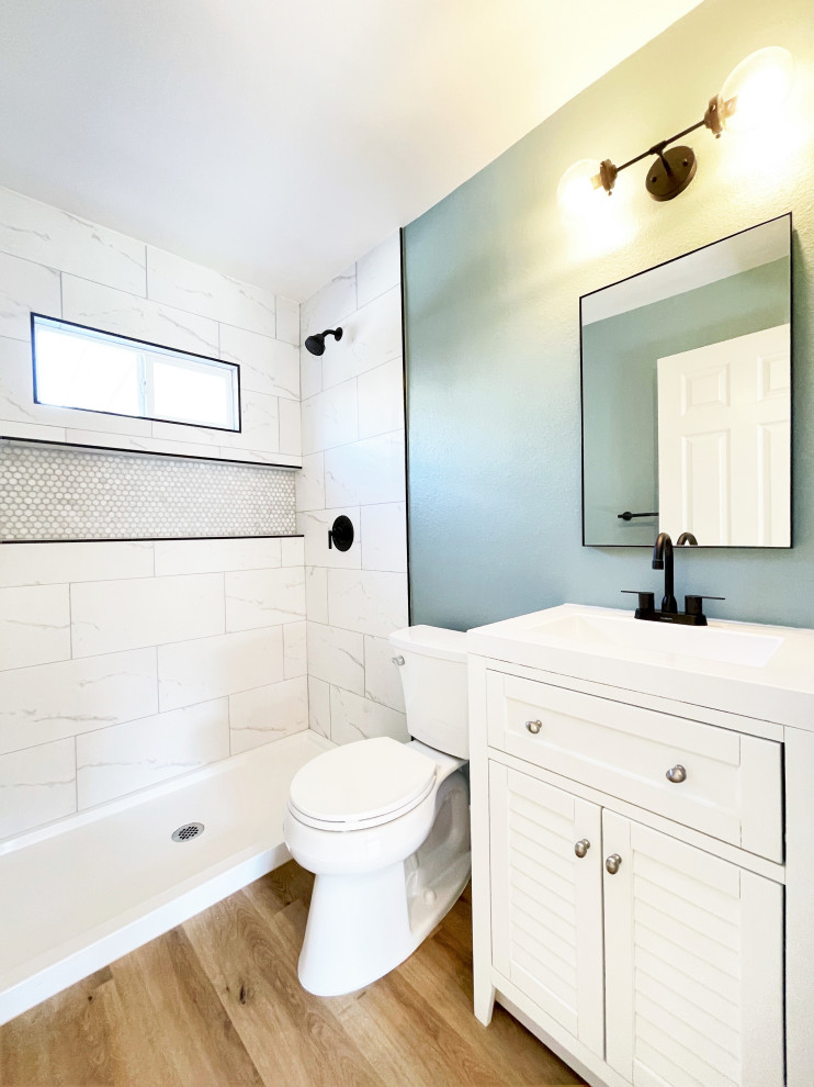 This is an example of a small modern bathroom in San Diego with louvered cabinets, white cabinets, an alcove shower, a two-piece toilet, white tiles, porcelain tiles, blue walls, vinyl flooring, an integrated sink, engineered stone worktops, beige floors, a shower curtain, white worktops, a wall niche and a single sink.