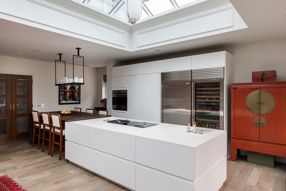 Large contemporary open plan kitchen in London with an undermount sink, flat-panel cabinets, white cabinets, stainless steel appliances, porcelain floors, with island, brown floor and white benchtop.