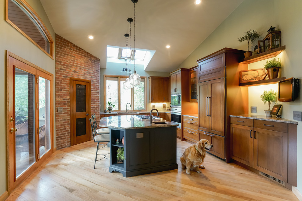 Example of a mid-sized transitional medium tone wood floor and brown floor kitchen design in Denver with a farmhouse sink, recessed-panel cabinets, medium tone wood cabinets, granite countertops, paneled appliances and an island
