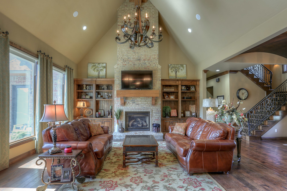 Inspiration for a large traditional open concept living room in Oklahoma City with beige walls, dark hardwood floors, a standard fireplace, a brick fireplace surround, a wall-mounted tv and brown floor.